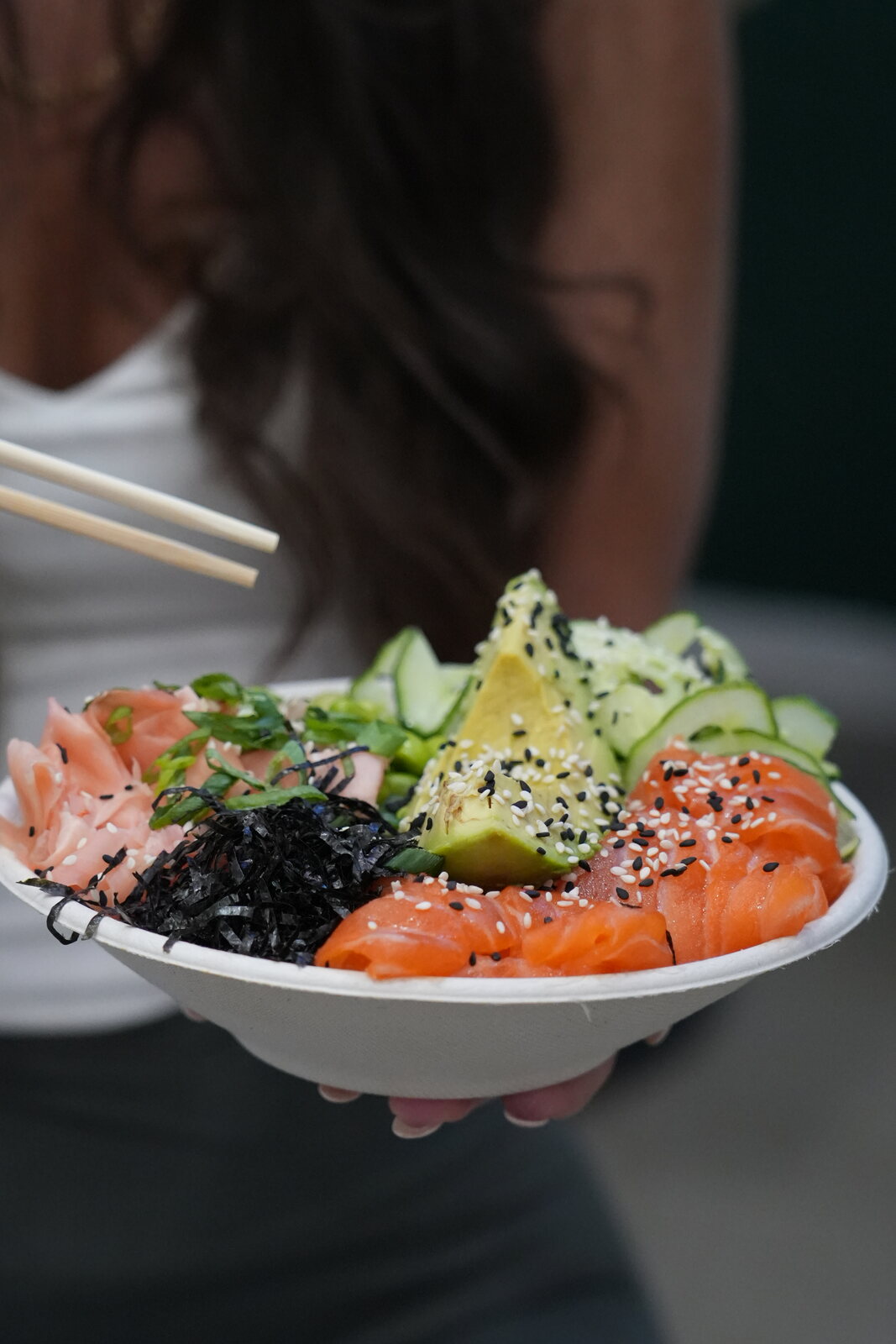 Fresh Pokenom salmon poke bowl held with chopsticks